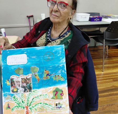 A woman wearing red glasses holds up her art work Image