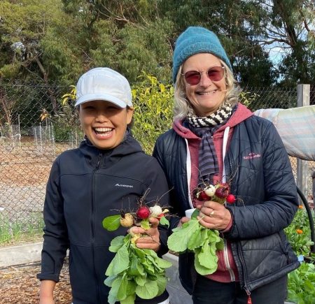 two women holding produce standing next to a scarecrow Image