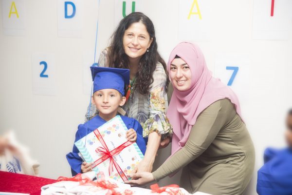 two women and a young child posing for the camera. the child is in a graduation outfit holding a gift