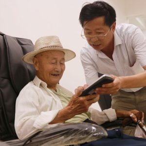 elderly man with a carer looking at mobile