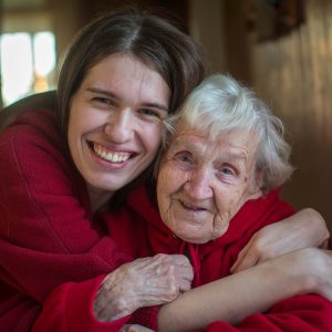 adult woman hugging an elderly woman while smiling at camera
