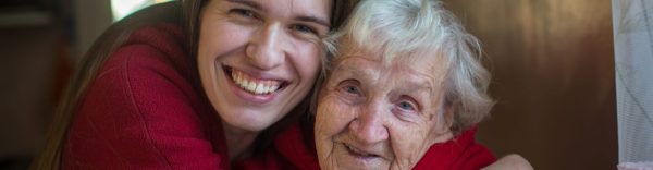 adult woman hugging an elderly woman while smiling at camera