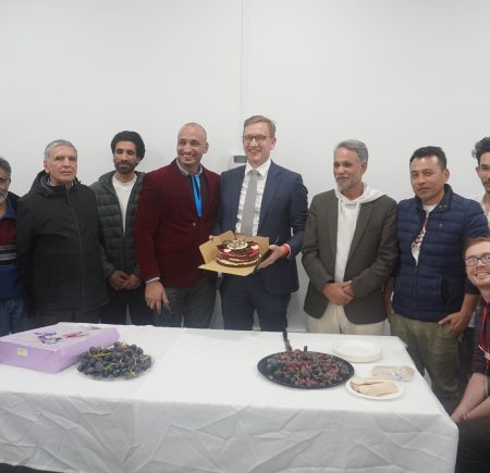 Group of men standing behind a table with dessert on it Image