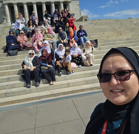 Najma is taking a selfie with a group of women behind her Image