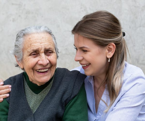 A young woman and an elderly woman smile together