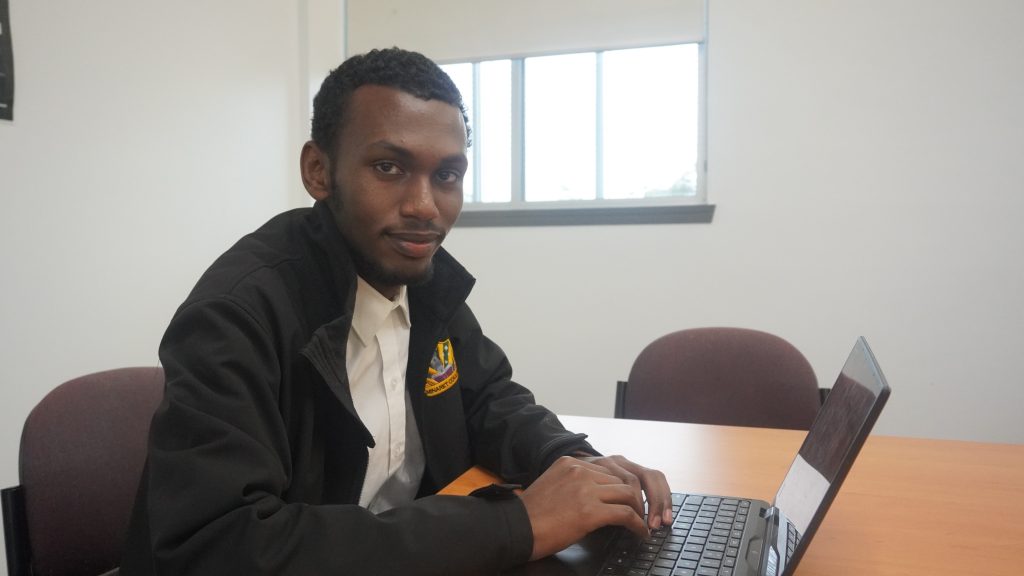 Abdul is typing on his computer and smiles at the camera