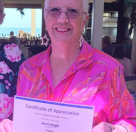 A lady holds up a 'certificate of appreciation' and smiles for a photo Image