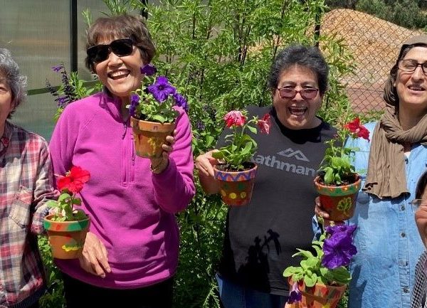 Group of smiling older women holding flowers, showcasing community involvement and support.