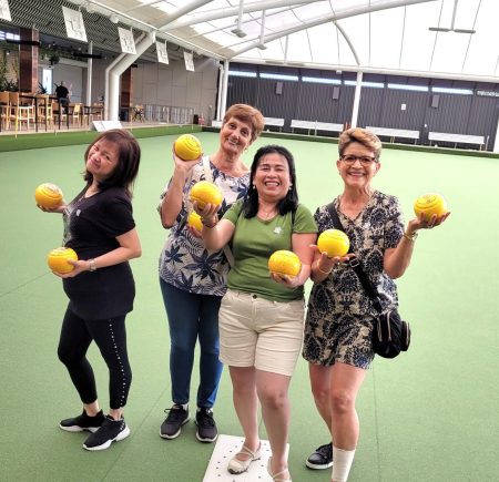 Four winners of the competition hold lawn bowls and smile at the camera Image