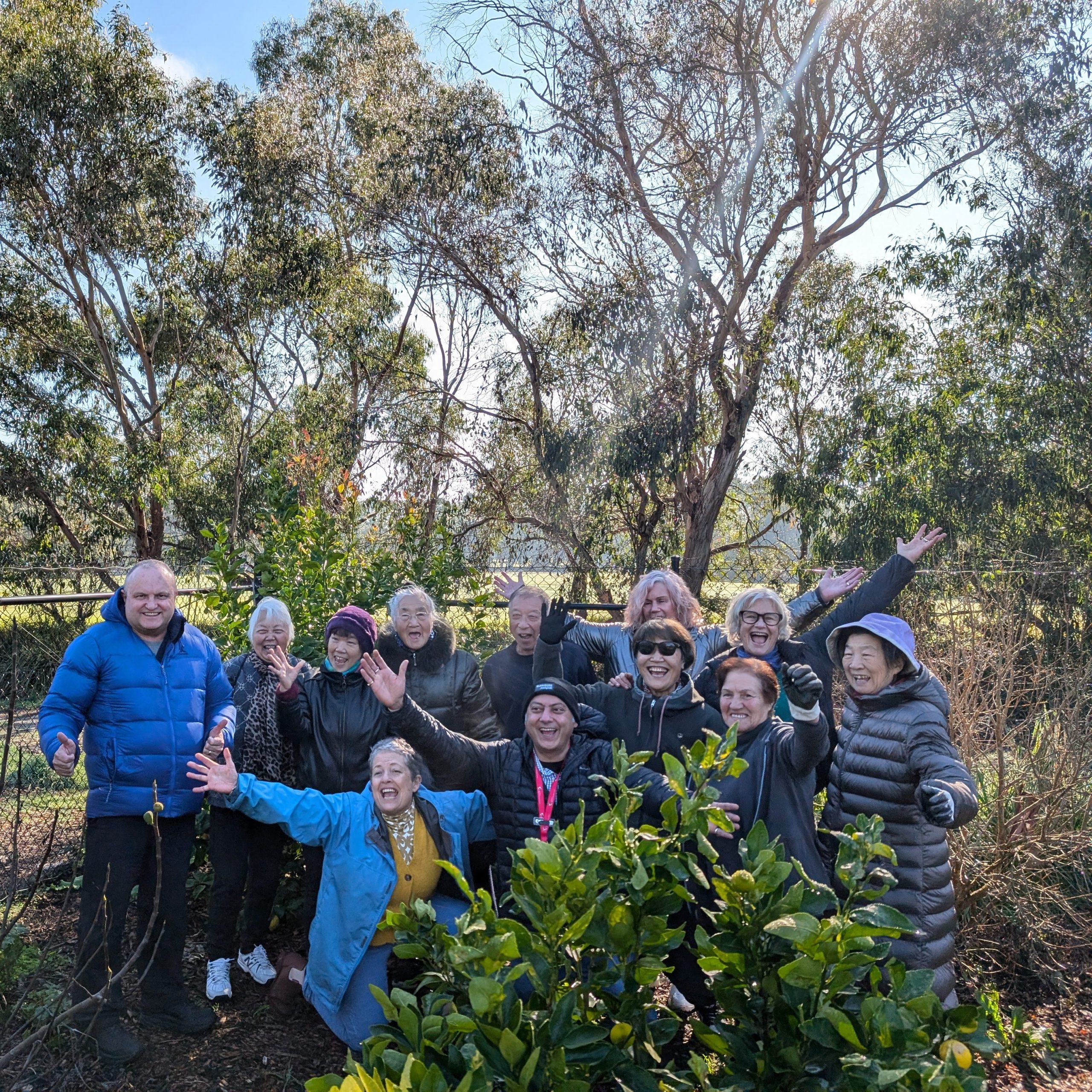 Visitors and clients pose together for a joyful photo. There are trees in the background and a green bush in the foreground.