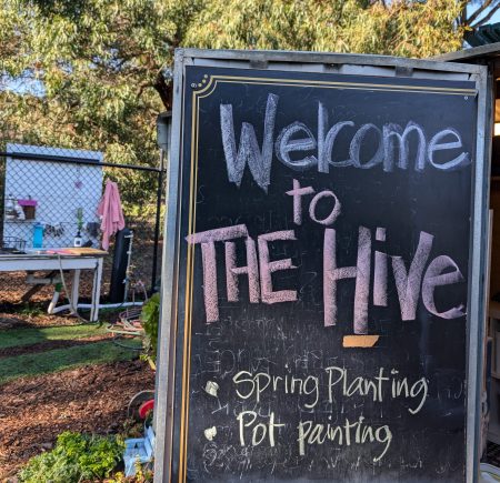 A black chalkboard sign writes 'Welcome to The Hive. Spring planting. Pot painting