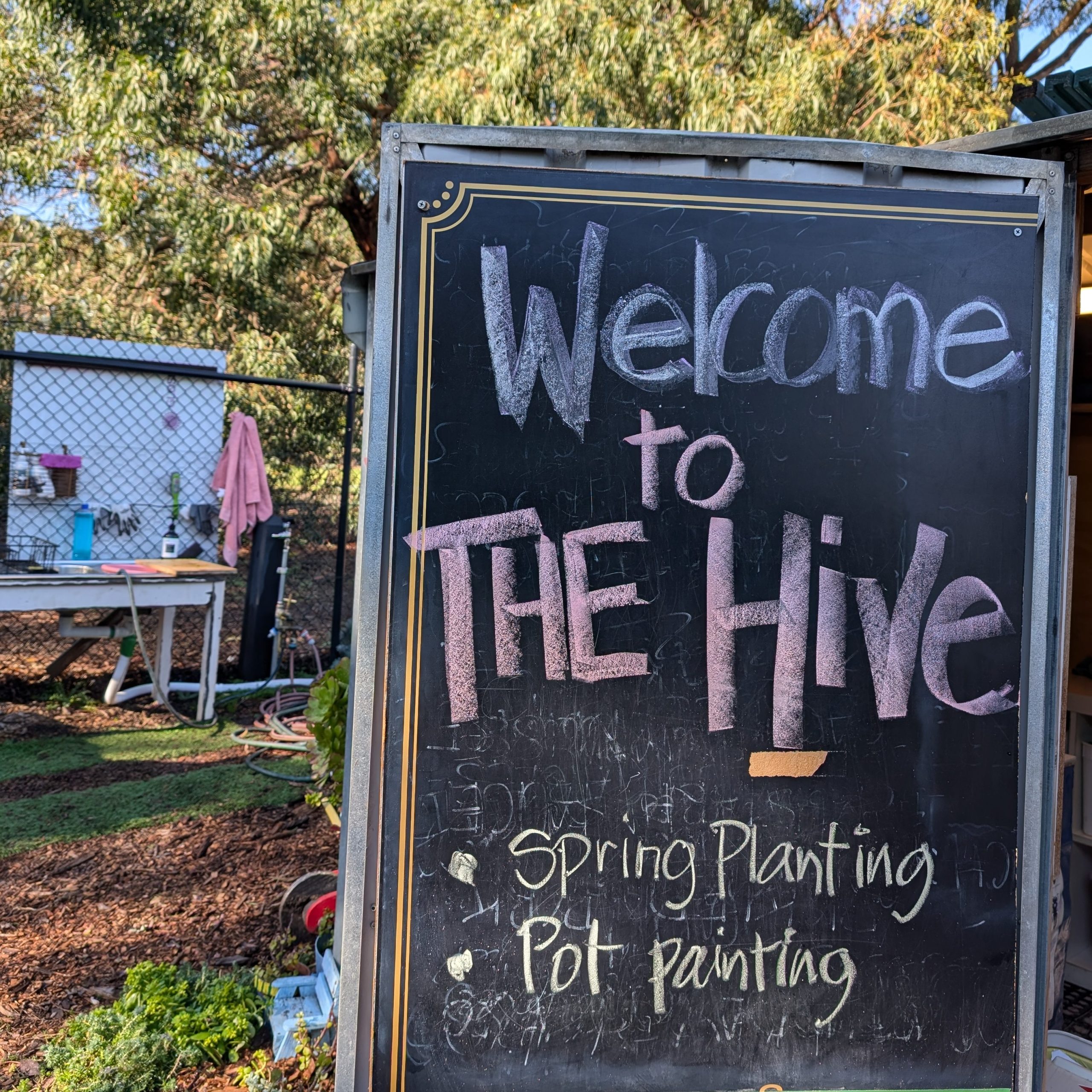 A black chalkboard sign writes 'Welcome to The Hive. Spring planting. Pot painting