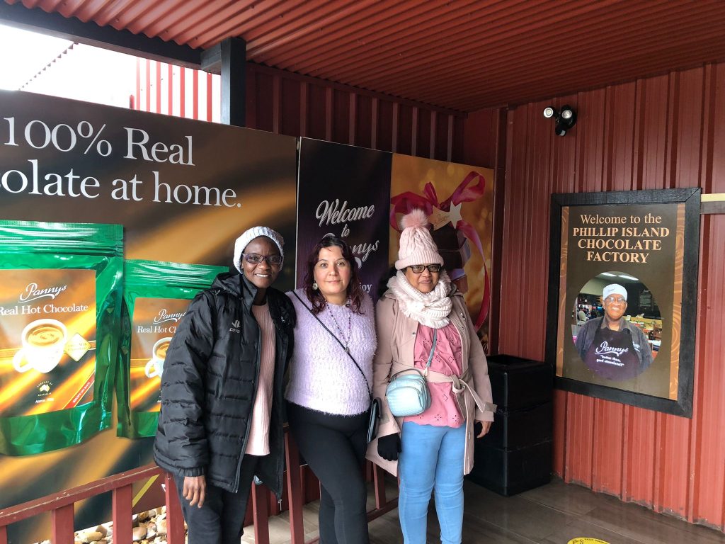 Three women stand outside the entrance to the Philip Island Chocolate Factory signage.