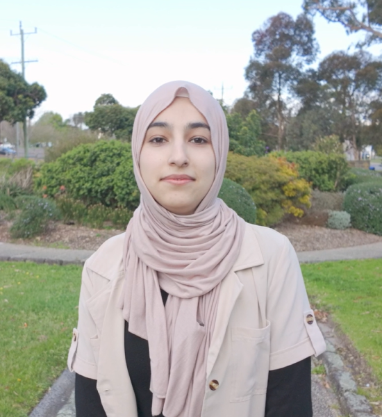 Arzo looks softly at the camera. She is wearing a beige head scarf and jacker