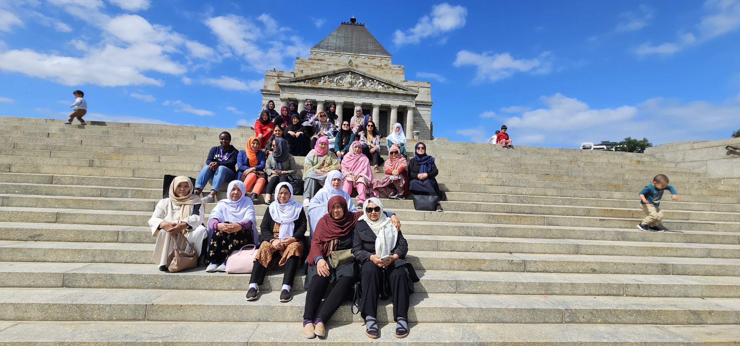 A group of women sit together on the steps of the Shrine of Remembrance