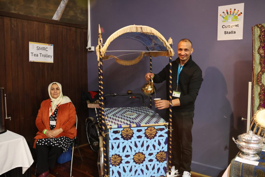 A man stands next to an Afghan tea trolley and serves tea.