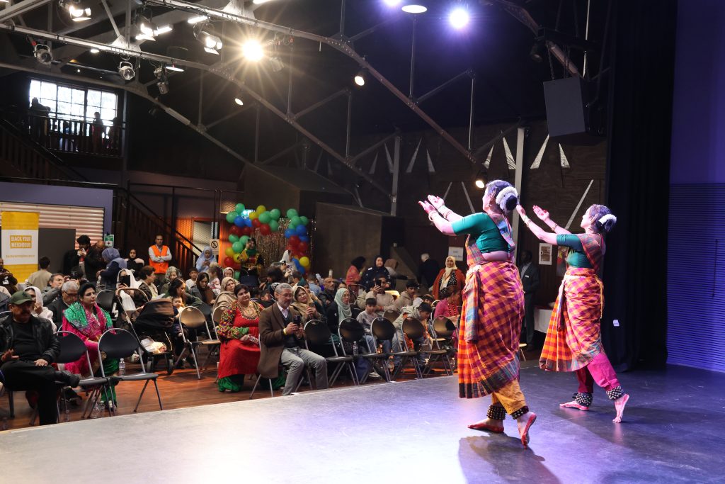Two girls dance on a stage and the crowd watches them