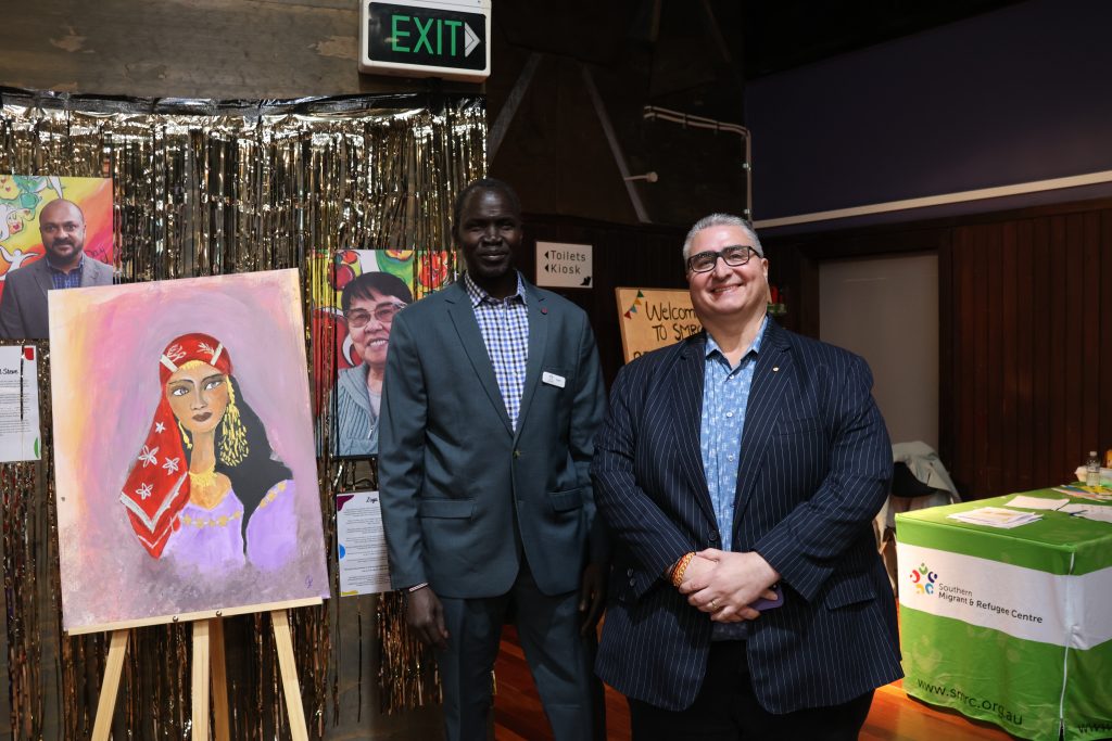 Two men smile at the camera. In the background are bright images and artwork