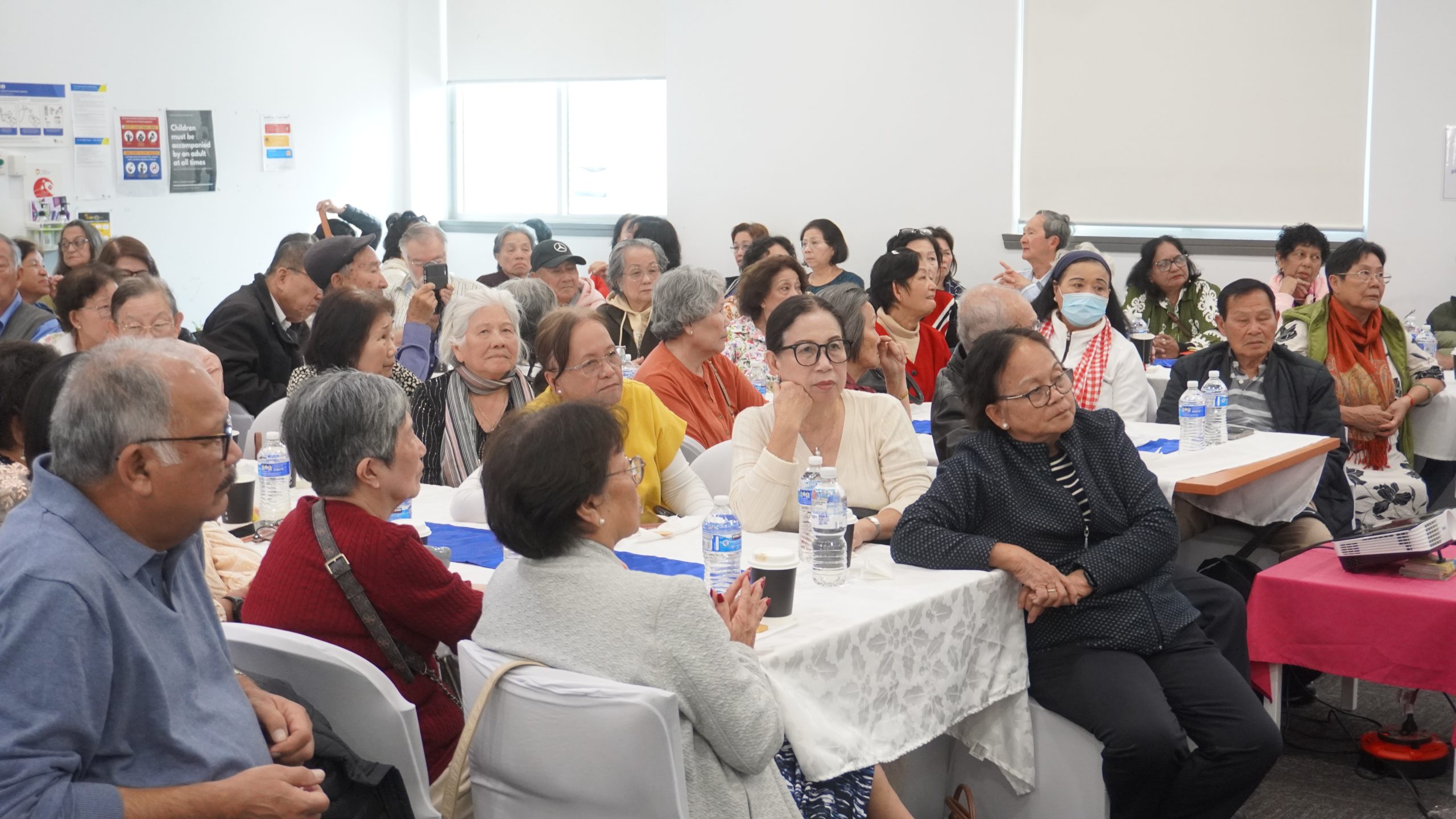 A group of older people gathered in a room watching a presentation off to the side